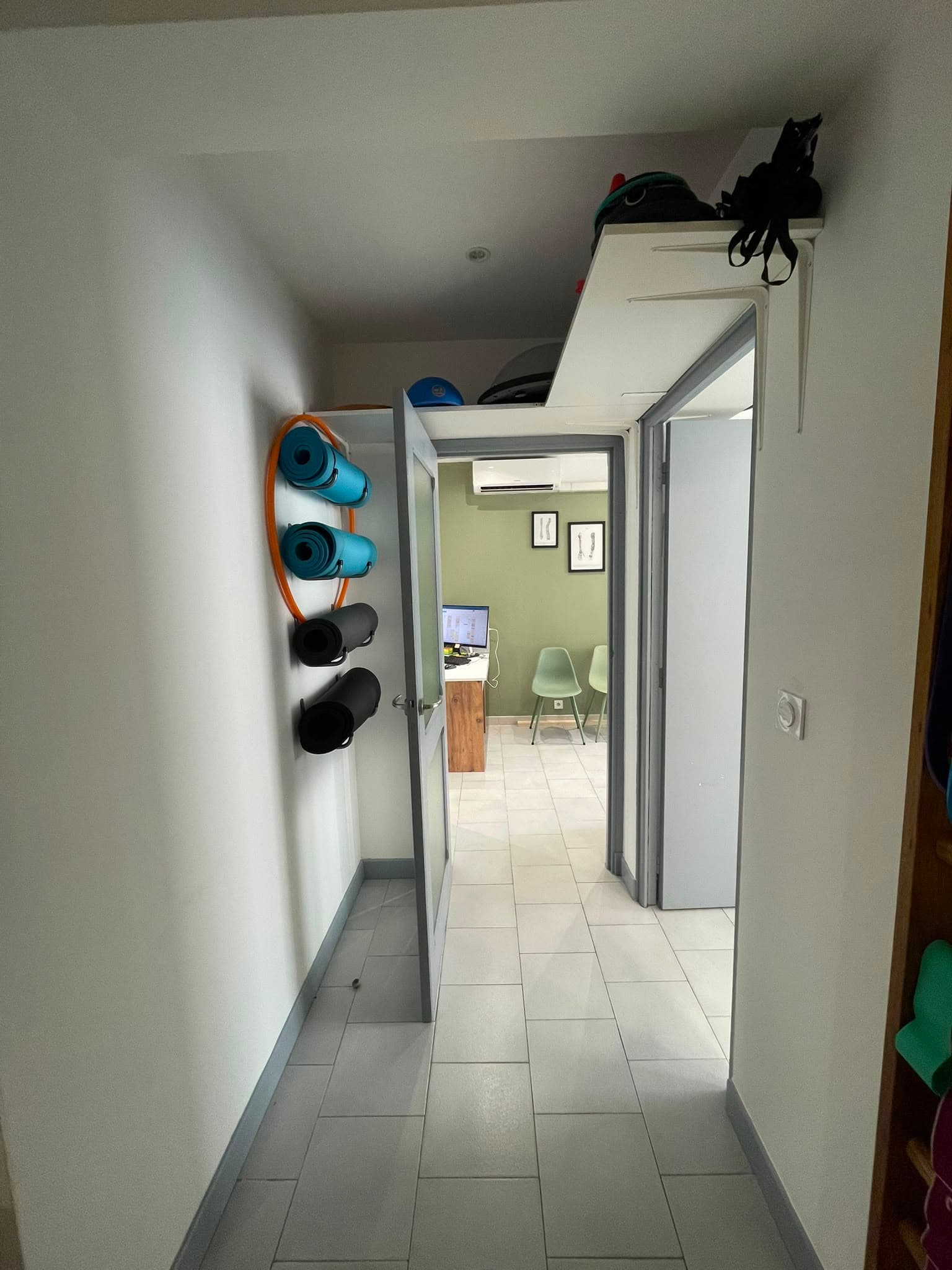 Couloir du cabinet avec tapis et matériel de rééducation rangés au mur
